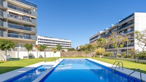 A rectangular swimming pool with a clear blue water surface, surrounded by a well-maintained lawn and a low stone wall. - Apartment with pool and parking 350m beach (Cambrils)
