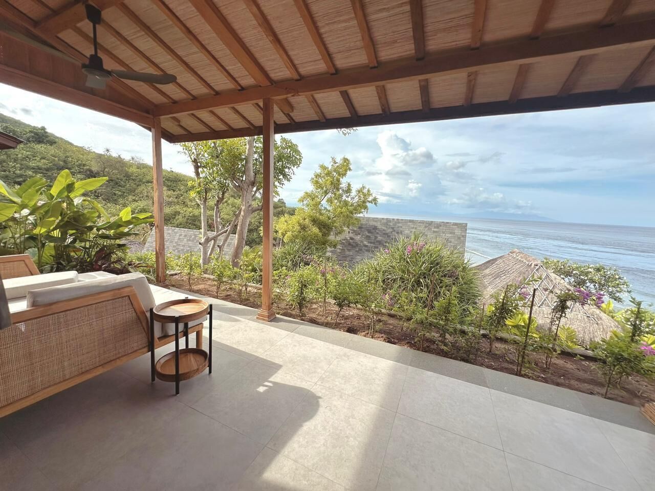 Un espace extérieur abrité, avec des sièges, offrant une vue sur la mer, un plafond en bois et une petite table.