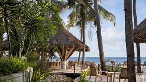 A tropical resort with thatched-roof structures, palm trees, and a wooden deck with lounge chairs. - Semaya Beach Resort (Penida Island)