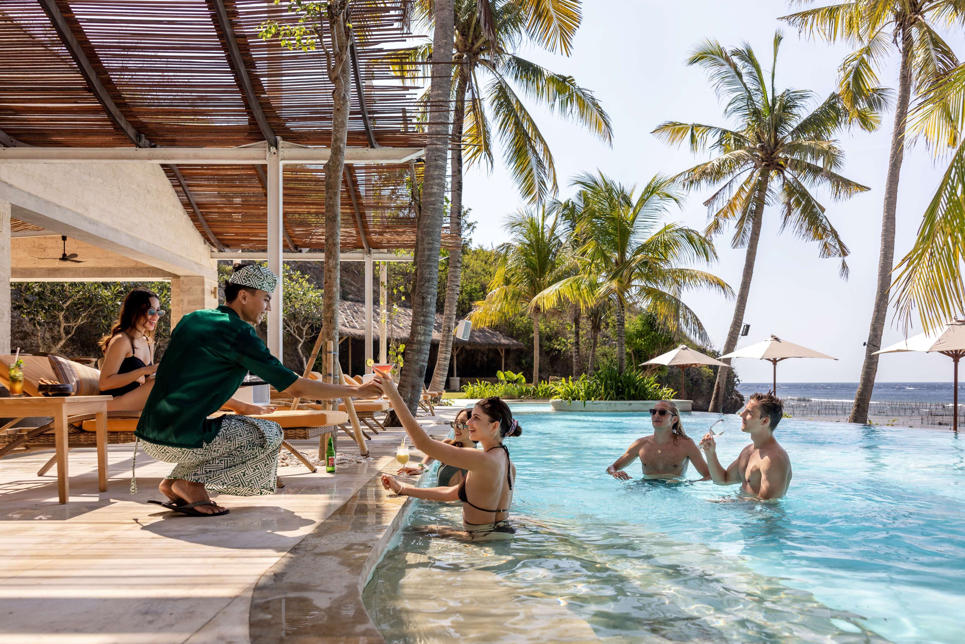 A poolside area with lounge chairs, a covered seating area, and palm trees.