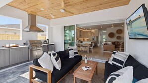 Une cuisine moderne équipée d’un barbecue, un coin repas avec un canapé noir et une table basse, et une vue sur la mer par une grande fenêtre.