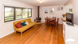 A cozy living room with a sofa, a dining table with chairs, a TV, and a wood-burning stove.