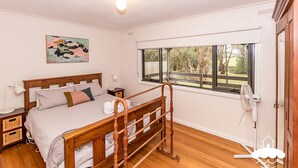 A bedroom with a wooden bed, a nightstand, a bedside table, a window with a view of the outdoors, and a ceiling fan.