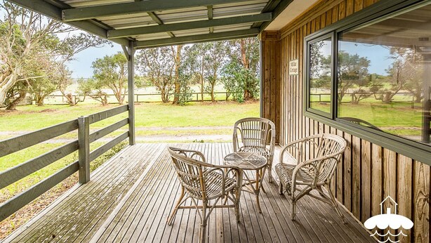 A covered outdoor area with a wooden deck, wicker chairs, and a table.