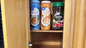 Un mueble de cocina con tres recipientes: crema para café French Vanilla, crema para café Caramel Macchiato y café instantáneo Nescafe Cálisico.