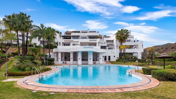 A resort with a swimming pool, palm trees, and a white building with multiple balconies. - Lomas de La Quinta | Modern Sea View Apt (Benahavís)