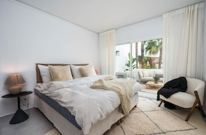 Une chambre à coucher avec un lit, une table de chevet, une lampe et une vue sur l’extérieur.