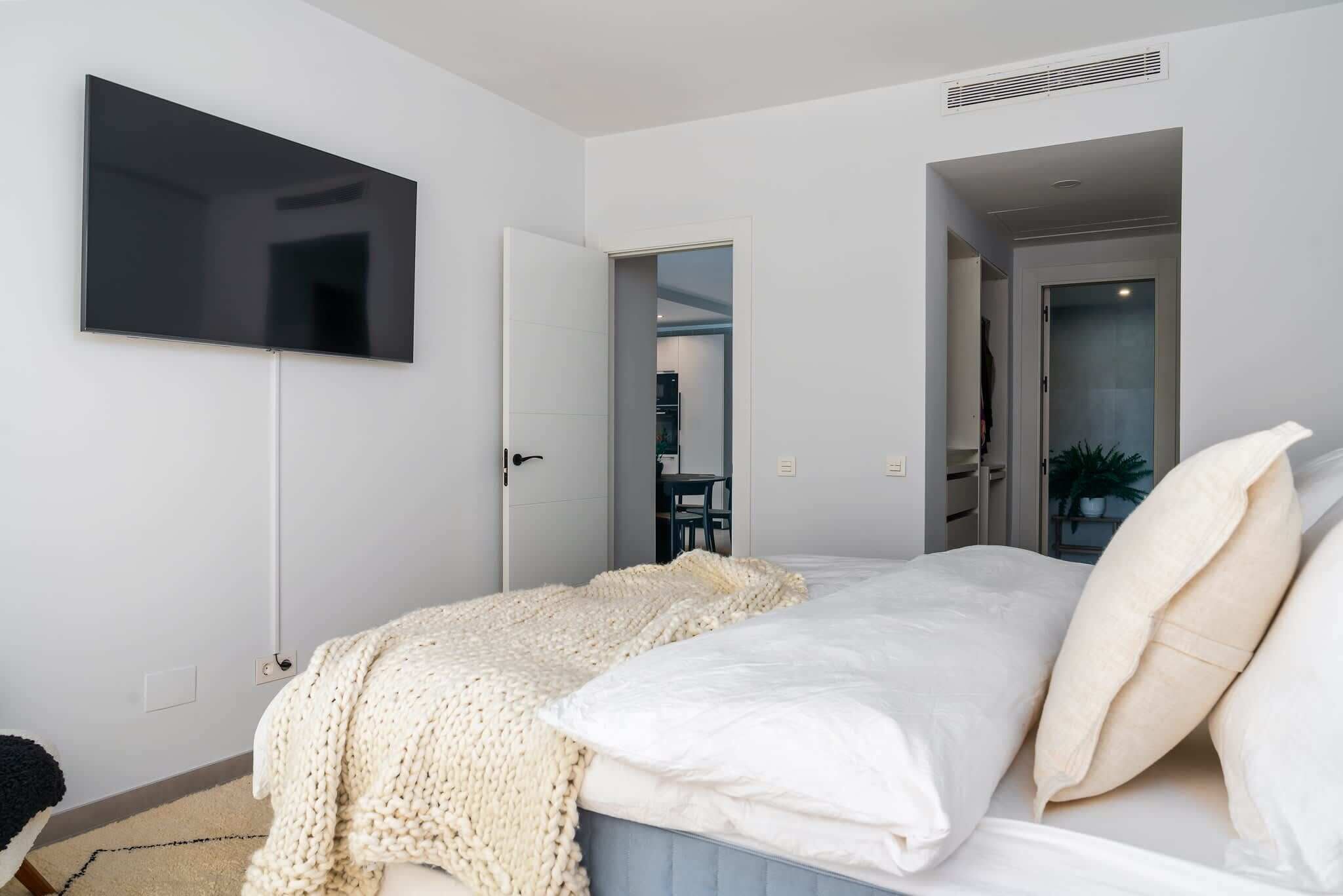 A bedroom with a bed, a TV mounted on the wall, and a door leading to another room.