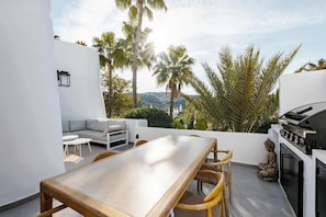 Une terrasse sur le toit équipée d’une table à manger, de chaises, d’un canapé, d’un barbecue et d’une statue de Bouddha.