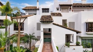 A white building with a tiled roof, a central staircase, and surrounding greenery. - Lomas de La Quinta | Modern Sea View Apt (Benahavís)