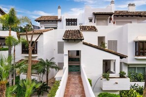 A white building with a tiled roof, a central staircase, and surrounding greenery.