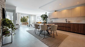 A modern kitchen with a dining area, large windows, and a view of palm trees. - Lomas de La Quinta | Modern Sea View Apt (Benahavís)