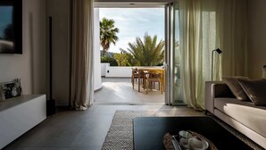 A modern living room with a sofa, a coffee table, and a view of an outdoor balcony with a table and chairs. - Lomas de La Quinta | Modern Sea View Apt (Benahavís)