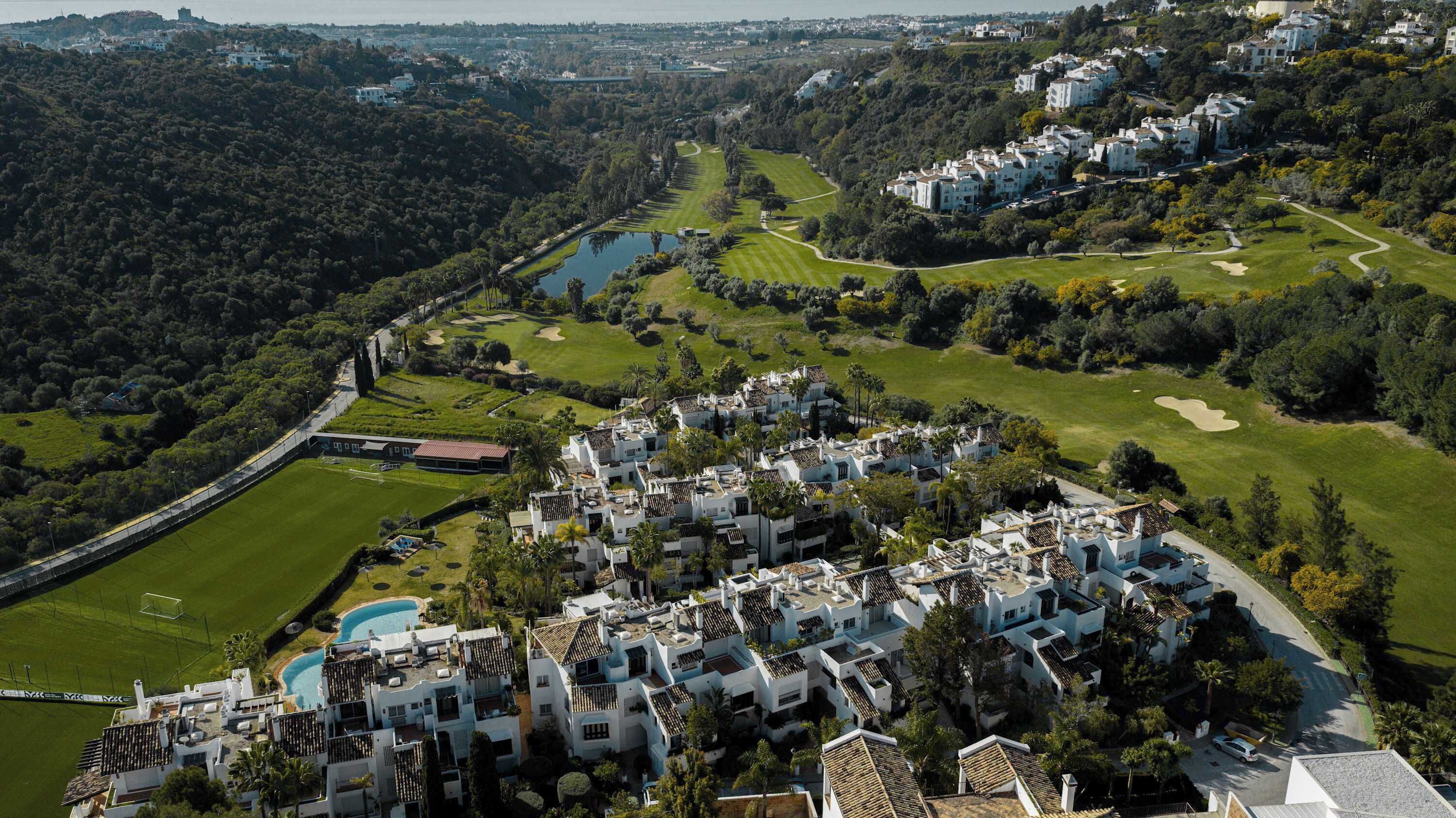 A residential area with white buildings, a golf course, and a body of water.