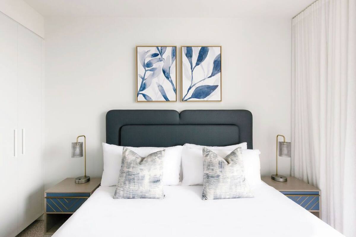 A neatly made bed with white and patterned pillows, a dark headboard, and two bedside tables with lamps.