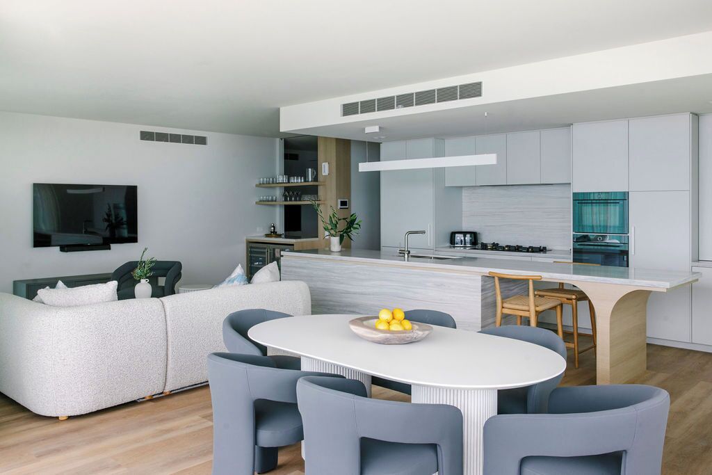 Una sala de estar moderna con sofá, una mesa de comedor con sillas, una cocina con isla central y un televisor de pantalla plana montado en la pared.