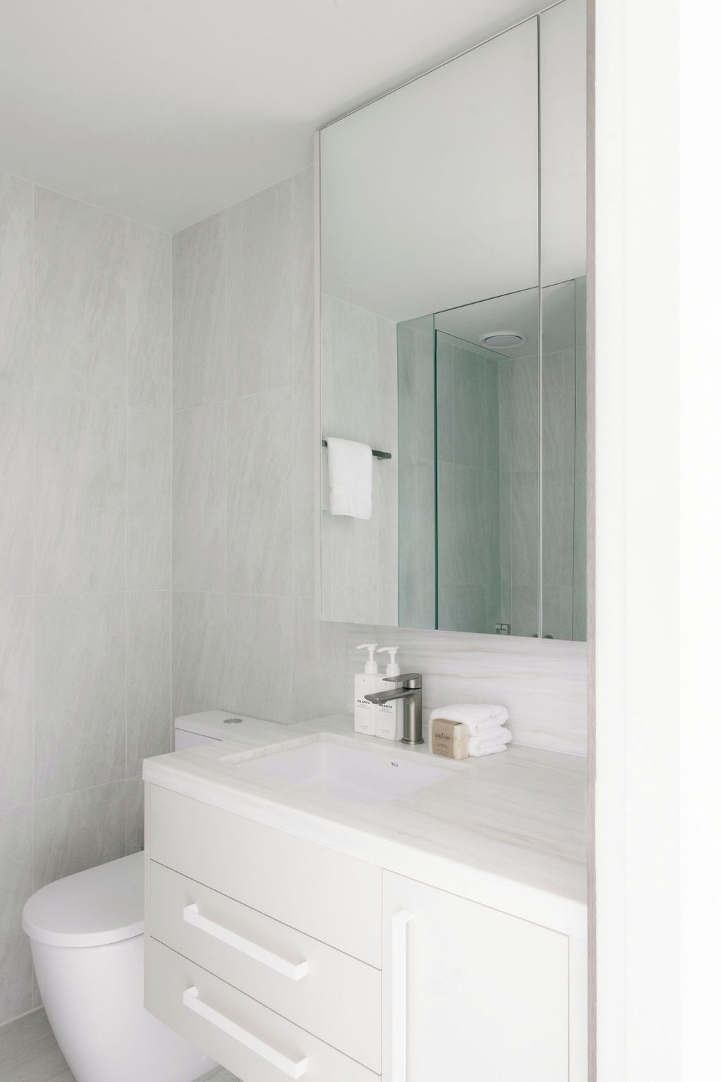 Un bagno moderno con un water bianco, una cabina doccia in vetro e un grande specchio sopra un mobile lavabo bianco con lavandino e cassetti.