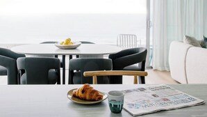 A dining area with a table, chairs, a bowl of lemons, a croissant, and a newspaper. - Kirra Point Holiday Apartments (Coolangatta)