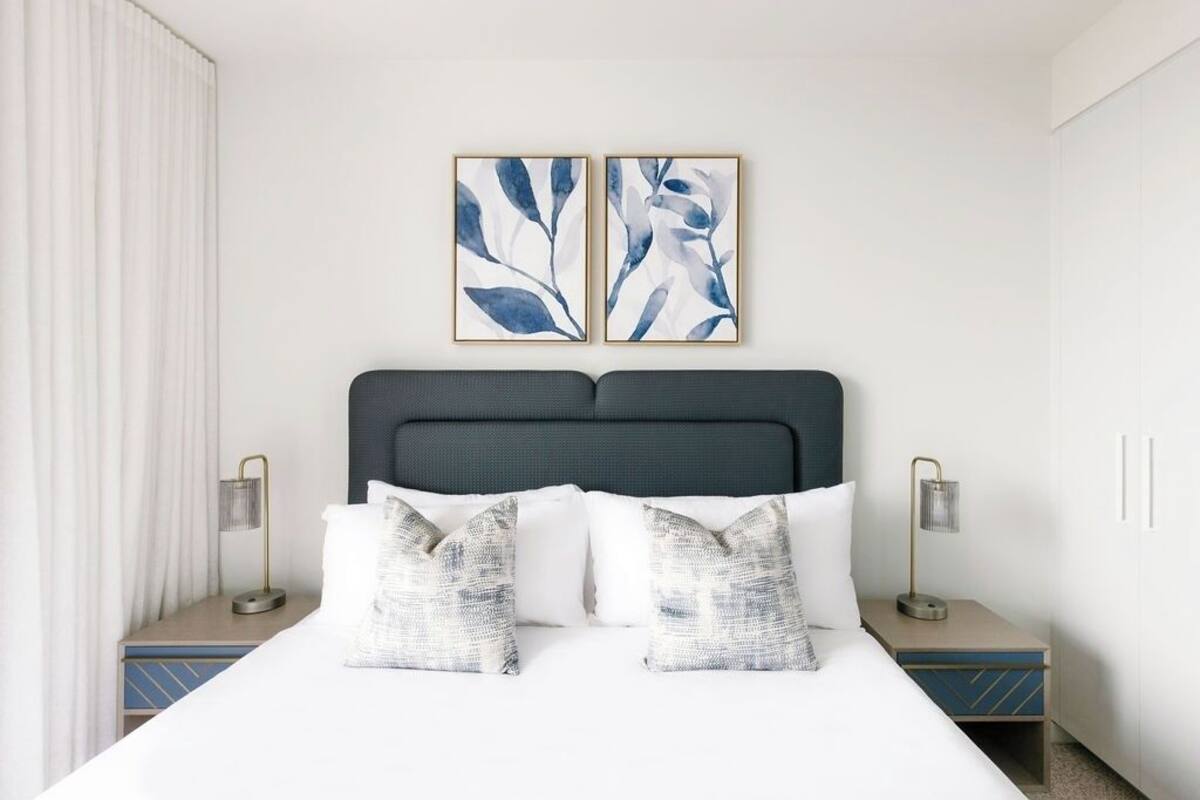 A hotel room with a bed, two nightstands, a headboard, and two wall-mounted paintings.