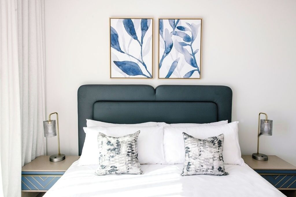 Een keurig opgemaakt bed met witte lakens en twee decoratieve kussens, een donker hoofdbord en twee nachtkastjes met lampen.