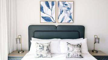 Een keurig opgemaakt bed met witte lakens en twee decoratieve kussens, een donker hoofdbord en twee nachtkastjes met lampen.