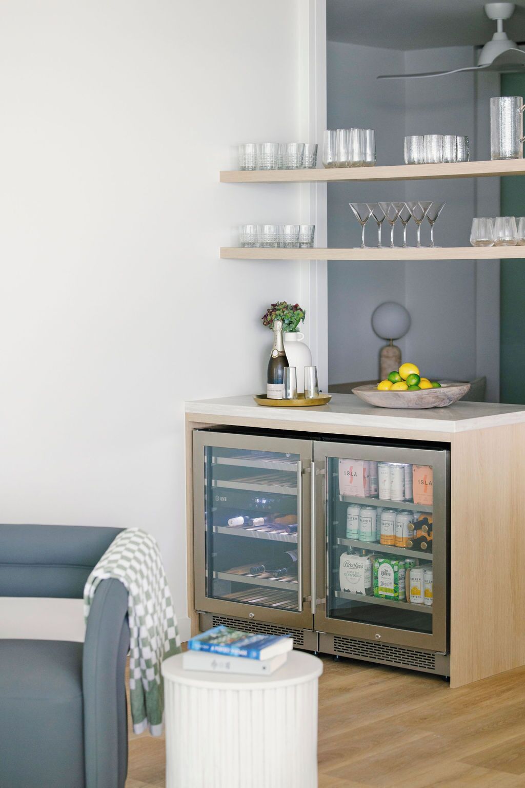 Une cuisine moderne dotée d’un réfrigérateur encastré, d’un plan de travail en bois et d’une étagère où sont posés des verres et un vase.