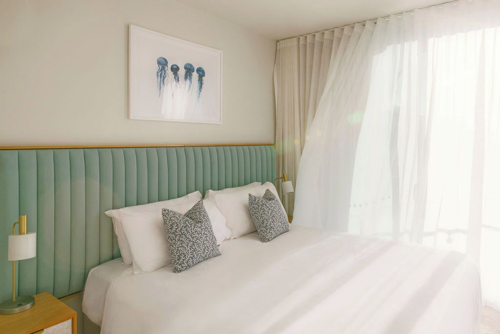 A hotel room with a bed, pillows, a nightstand, a lamp, and a framed picture on the wall.