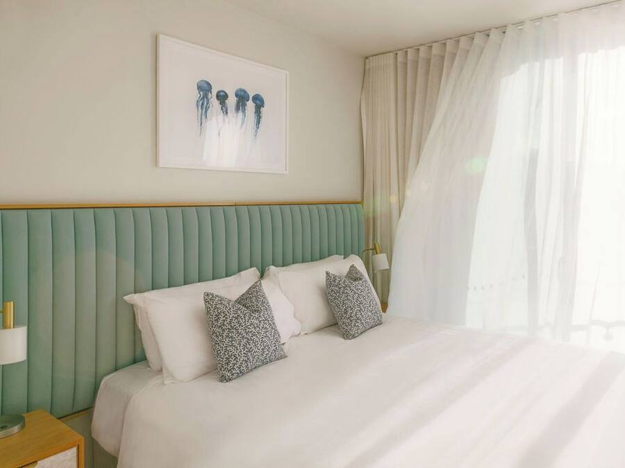 A hotel room with a bed, pillows, a nightstand, a lamp, and a framed picture on the wall.