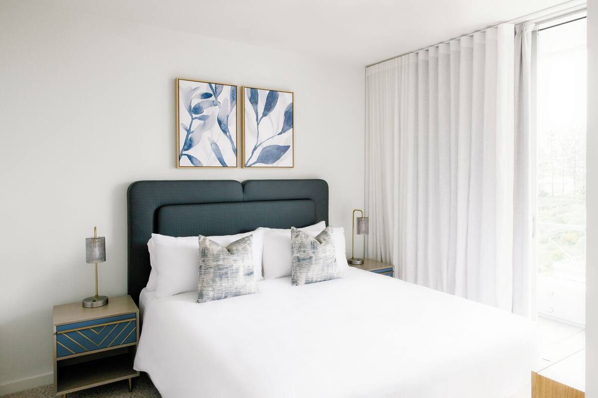 A neatly made bed with white linens and decorative pillows, a dark headboard, and two bedside tables with lamps.