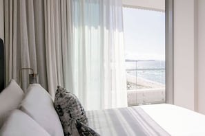 A bedroom with a bed, white curtains, and a view of the beach.