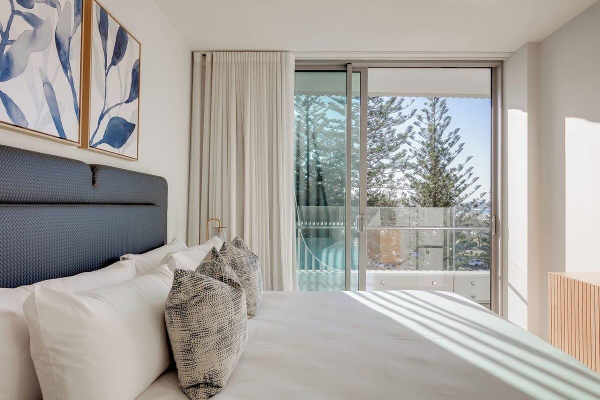 A bedroom with a bed, a large window, and a view of trees.