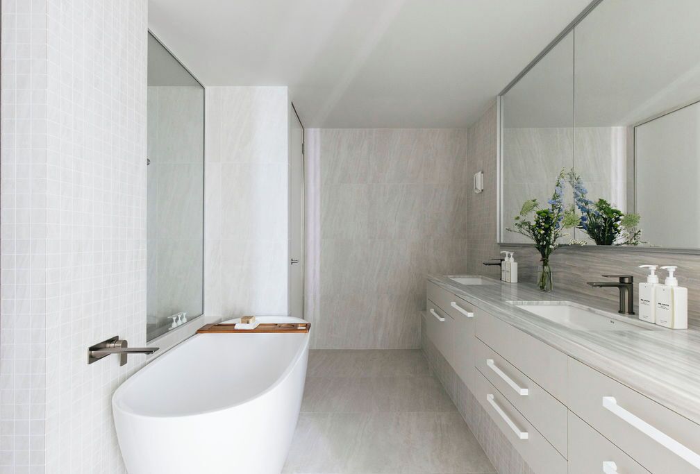 Un baño moderno con una bañera independiente, un espejo grande y un tocador con encimera de mármol.
