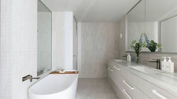 Un baño moderno con una bañera independiente, un espejo grande y un tocador con encimera de mármol.
