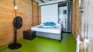 Een houten kamer met een bed, een ventilator en een groene vloer.