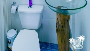 Een badkamer met een glazen wastafel, een wit toilet en een spiegel aan de muur.