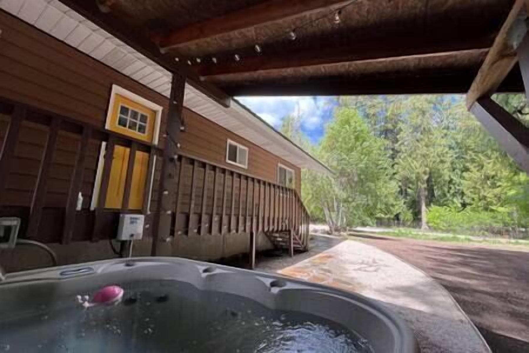 A wooden cabin with a hot tub and a covered patio area. - Vibrant Forest Retreat | Game Room, Spa, Fire Pit - Sleeps10 (Spirit Lake)