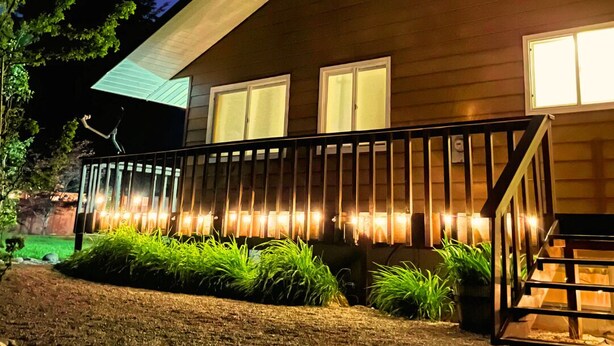 A modern house with a wooden exterior, a covered porch with lights, and a well-maintained garden. - Vibrant Forest Retreat | Game Room, Spa, Fire Pit - Sleeps10 (Spirit Lake)