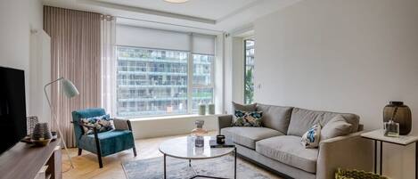 Un salon moderne comprenant un canapé, un fauteuil, une table basse et un téléviseur.
