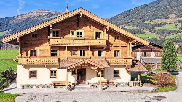 Eine große Holzhütte mit mehreren Balkonen, einem Steinfundament und einer malerischen Bergkulisse.
