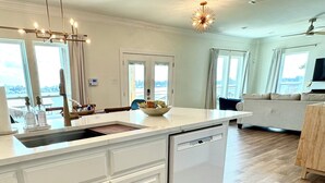 A modern kitchen with white cabinetry, a dishwasher, and a large island with a sink. - It's About River Time, a 3BR/3BA house on False River, fenced yard & large pier! (Jarreau)