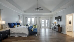 A spacious bedroom with a large bed, a sofa, a ceiling fan, and a TV. - It's About River Time, a 3BR/3BA house on False River, fenced yard & large pier! (Jarreau)