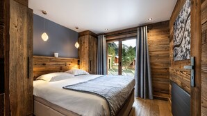 A bedroom with a wooden headboard, a bed with white linens, a view of the outdoors through a large window, and a wooden wall with a textured design. - N°2: Beautiful 10 people apartment with sauna  et  south facing terraces (CHAMPAGNY EN VANOISE)