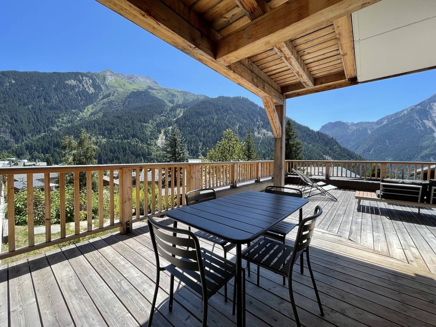 A wooden deck with a table and chairs, overlooking a mountainous landscape.