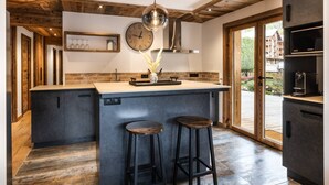 A modern kitchen with a central island, wooden ceiling beams, a large clock, and a view of the outdoors. - N°2: Beautiful 10 people apartment with sauna  et  south facing terraces (CHAMPAGNY EN VANOISE)