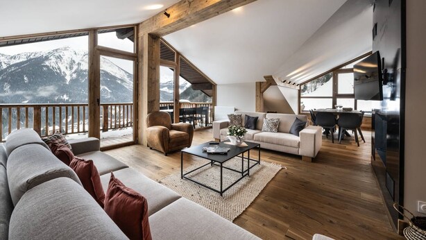 A spacious living area with a large window overlooking a snowy mountain, a cozy seating arrangement, and a modern kitchen.