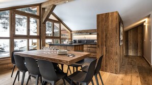 A modern kitchen with wooden beams, a large dining table with chairs, and a view of a snowy landscape.