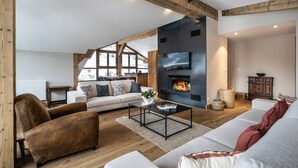 A spacious living room with a fireplace, wooden beams, and a large window overlooking a snowy landscape.