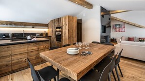 A modern kitchen with wooden cabinets, a dining table with chairs, and a living area with a sofa and artwork.
