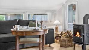 A cozy living room with a sofa, a table with a candle, a lamp, and a wood-burning stove. - 2 bedroom nice home in Højby (Højby)