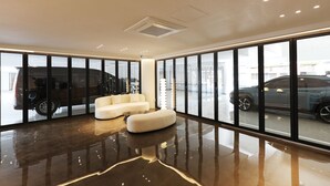 Un intérieur moderne avec un sol réfléchissant, un canapé blanc et de grandes fenêtres donnant sur les voitures garées à l’extérieur.